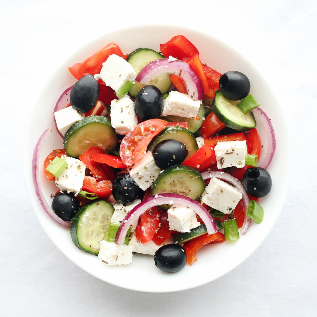 A bowl of salad with cucumbers, tomatoes and olives.